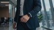 © Oak - Close-up of a businessman in a suit checking his smartwatch while walking in a modern office corridor. This image highlights the use of wearable technology for productiv