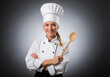 © Kamran - A confident and professional female chef in uniform, holding wooden spoons with arms crossed against a dark, dramatic background