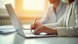 © Bakreen - Close up of woman's hands typing on laptop keyboard another person in the background Documents and pen nearby