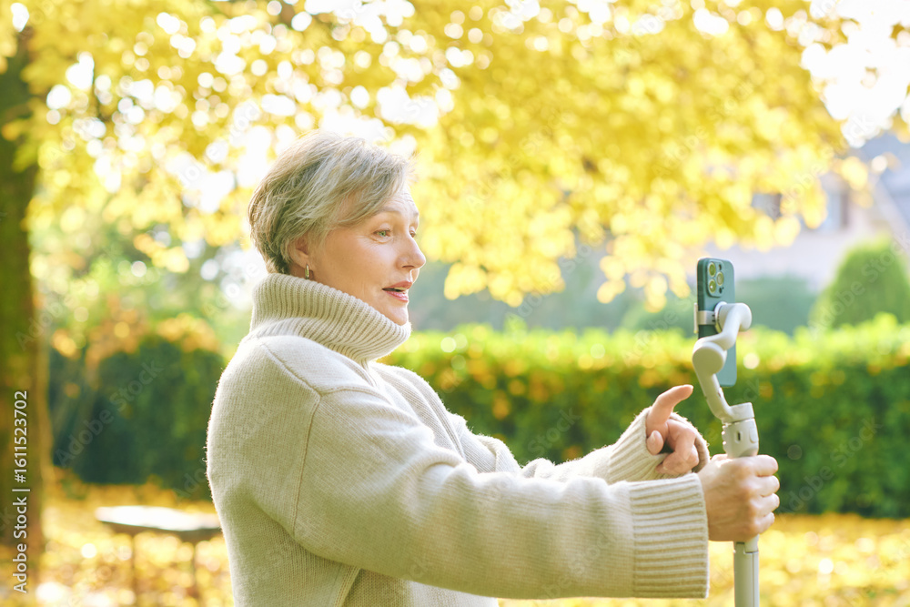 Outdoor portrait of happy and active mature woman recording herself ...
