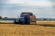 © Adam - Grain combine harvester working in a field during harvest season. Rear view with farm buildings and rural landscape in the background.