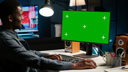 Poster - African american remote worker sitting at desk with isolated copy space at his home workstation, looking at pc screen and solving his daily tasks. Young adult browsing the web. Camera A.