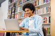 © Home-stock - Happy Black male university student preparing for lecture, using laptop while studying in college library, using modern wireless tech and internet resources