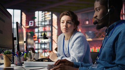 Poster - Manager supervising technical support specialist in call center office doing troubleshooting. Supervisor overseeing work done by IT worker fixing customer connectivity issue, camera B