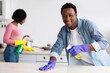 © Prostock-studio - Cheerful young black guy and lady cleaning their new house together, rubbing tables with dust cloth, using sprays, kitchen interior. African american family house-keeping at weekend, copy space