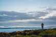 © Quincy - Scenic view of a man taking photos on the rocks at sea shore with tides and cloudy sky in the background, Griffiths Island, Port Fairy, Great Ocean Road, Victoria, Australia
