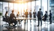 © Masa - Blurred image of businesspeople in a modern office, some seated at a conference table and others standing near large windows overlooking a city