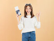 © sitthiphong - Happy smiling young Asian woman holding passport with plane tickets, credit card and shows ok sign in beige color background. Tourist travel trip journey concept.
