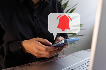 Poster - Person holding a cell phone while working in front of a computer with a virtual icon of a speech bubble and a red notification bell