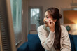 © Crystal - Young Asian woman applying foundation on her nose with a makeup brush, sitting on a sofa in her living room, getting ready to go out, taking care of her appearance with a beauty routine