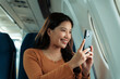 © Crystal - Happy passenger smiling while capturing moments with her smartphone during a flight, relishing the journey and enjoying breathtaking views from the airplane window