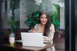 © Crystal - Smiling businesswoman using laptop and smartphone, managing her business remotely while enjoying a refreshing drink in a stylish cafe with green plants