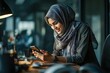 © nana - Middle Eastern muslim businesswoman manager ceo using cell phone mobile app. Smiling young indian woman in hijab holding smartphone sitting in office working online at desk on gadget with copy space.