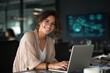 © nana - Portrait at camera smiling latin female marketing manager, professional it specialist working at laptop computer sitting at desk in modern office. Cheerful young woman employee using pc for business