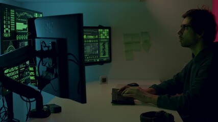 Male programmer working intently at a modern workstation with multiple screens displaying data and graphics, immersed in a high-tech environment showcasing digital innovation