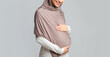 © Prostock-studio - Pregnancy Concept. Unrecognizable pregnant islamic woman in hijab touching her belly, posing over gray background, panorama with free space