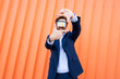 © VISTA by Westend61 - Businessman with VR glasses gesturing on orange background outdoors