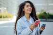 © VISTA by Westend61 - Woman smiling outdoors using smartphone and credit card for online shopping