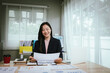 © Kieng - A focused businesswoman works at her desk, analyzing charts and graphs on a monitor, surrounded by documents, showing productivity, strategy, and success in a modern office environment.