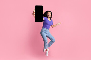 Happy asian young woman showing empty smartphone screen while jumping up over pink studio background, collage, full size photo. Excited lady recommending nice and useful mobile application