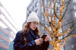 Woman using smart phone near tree decorated with string lights in city