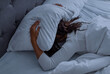 © Prostock-studio - Sleeping Problem. Stressed African American lady lying alone in bed covering head under pillow feeling afraid or depressed, suffering from insomnia or mental problems after breakup
