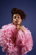 © Seventyfour - Vertical portrait shot of young adult woman posing confidently in fashion photoshoot, wearing voluminous ruffled garment, looking directly at camera against plain studio background