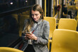 Smiling young woman using mobile phone sitting by window in tram