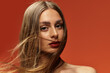 © LIGHTFIELD STUDIOS - Beautiful woman with long hair poses confidently against a vibrant orange backdrop