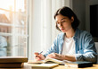 © imfotograf - A focused female student diligently studying for her exams in a sunlit room.