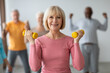 © Prostock-studio - Selective focus on cheerful senior lady posing with fitness tools, multiracial group of healthy elderly people in sportswear doing strength building workout with dumbbells at gym