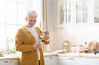 © Prostock-studio - Happy senior woman in casual outfit pouring spring water into glass in cozy kitchen, copy space. Smiling grey-haired grandmother with short haircut drinking water while cooking, home interior