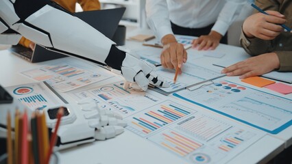 Poster - A robotic hand assists human team members in a modern office setting, collaborating on business analysis, charts, and data during a productive meeting.Noogenesis