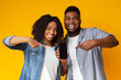 © Prostock-studio - New mobile app. Cheerful african american couple holding and pointing at smartphone with black screen for mockup, posing together on yellow background