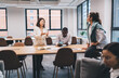 © BullRun - Asian woman and Black male colleague share ideas using a smartphone at a wooden table, symbolizing mobile technology use, digital collaboration, and smart teamwork in business context