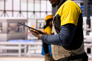 Poster - Industry 4.0 male engineer leverages a tablet to oversee and optimize automated systems in smart manufacturing plant. African american technician ensures seamless industrial automation.