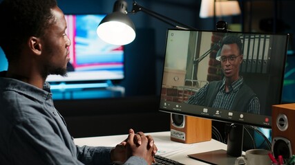 Poster - African American man enjoys video conferencing with manager at desk, discussing with his colleague online using a computer at home office setup. Young associates team meeting online. Camera B.