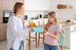 © Pixel-Shot - Happy mother giving school lunchbox and bottle of juice to her daughter in kitchen