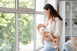 © Pixel-Shot - Young mother breastfeeding her baby near window at home