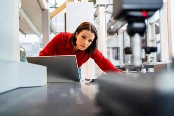 Concentrated engineer with laptop examining machine at factory