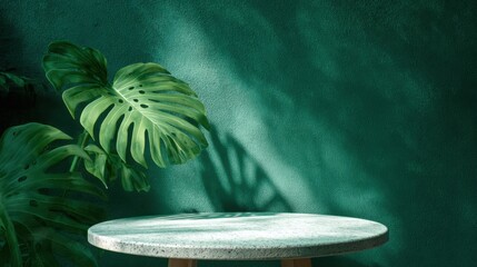 Poster - A round tabletop rests on a wooden base against a vibrant green wall, adorned with large tropical leaves casting intricate shadows. Soft light adds a calming atmosphere to the setting.