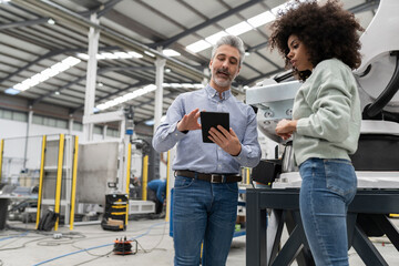 Engineer showing tablet PC to developer standing in factory