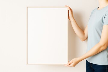Poster - Woman holding blank white poster frame against light wall background for mockup or advertising concept design template with copy space..
