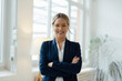 © BusinessClass by W61 - Happy businesswoman standing with arms crossed in office