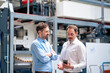 © BusinessClass by W61 - Businessman looking at smart phone and discussing with colleague in factory