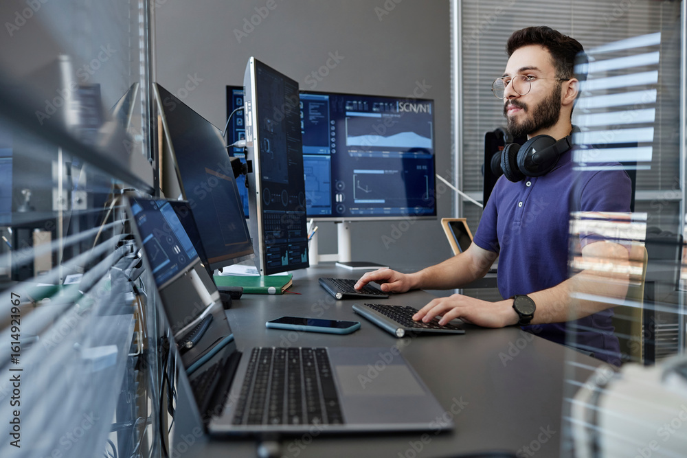 Young computer programmer with wireless headphones working on desktop ...