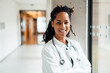 © BusinessClass by W61 - Happy young female doctor wearing lab coat leaning on column in hospital corridor