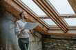 © BusinessClass by W61 - Thoughtful architect standing with blueprint looking through window at construction site
