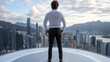 © siraphol - Confident businessman standing on skyscraper helipad overlooking city skyline and mountains
