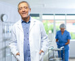 © JackF - Elderly, positive male doctor stands in middle of clinic office. Unrecognizable nurse in background cleans instruments